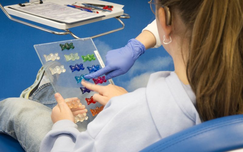 Farbmusterkarte in der Hand: Patientin sucht Lieblingsfarbe für ihre Zahnspange.