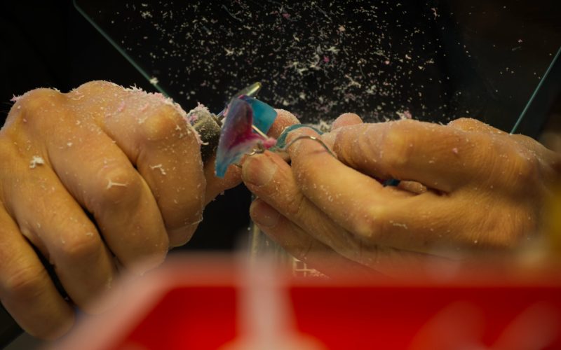 Zahntechniker fräst eine kieferorthopädische Apparatur; Metallspäne fliegen vom Fräser.